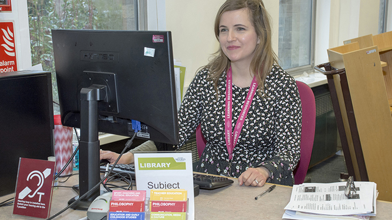 A member of Library staff sitting at the Harcourt Hill enquiry desk.